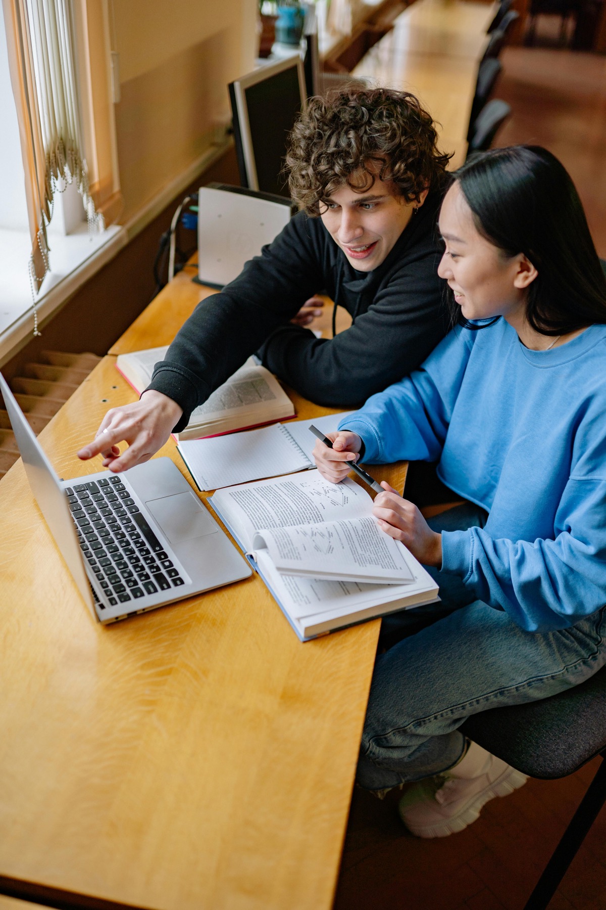 Two students studying together with a laptop and textbooks